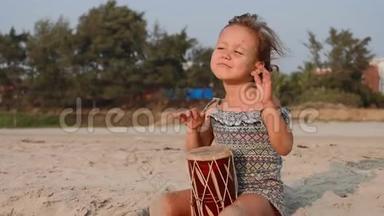 可爱的小女孩在沙滩上打鼓。