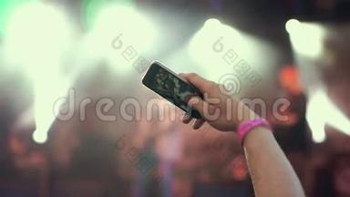 露天摇滚音乐会的人群聚会。 站在人群中的年轻女子手持智能手机拍摄视频