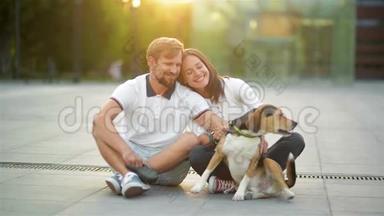 户外爱情情侣肖像欣赏夏日夕阳与比格狗坐在城市广场。