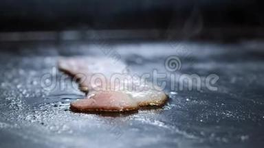 在热烤架上烤制的培根片。 一个厨师在专业的厨房里炸薯条，然后把培根切片