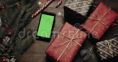 上景。 黑色智能手机与绿色屏幕躺在桌子上与圣诞节假日装饰。 圣诞老人的手