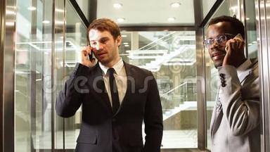 两名跨国商务人员站在<strong>电梯</strong>里使用智能手机。 大型<strong>玻璃电梯</strong>里的商务人士