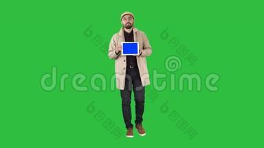 年轻人走着，说话，在绿色屏幕上显示带有蓝色屏幕模型的数字平板电脑，色度键。