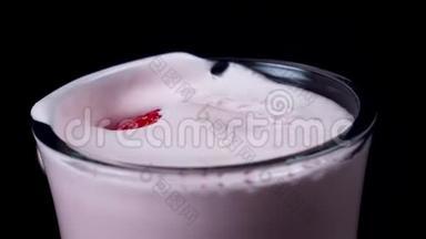 加草莓奶昔的杯子。 框架。 在鲜红色的奶昔里，把鲜红色的草莓放在黑色上