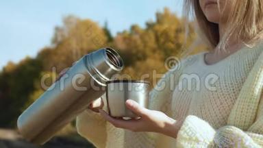 从热水瓶到杯子里倒热茶的年轻女子。