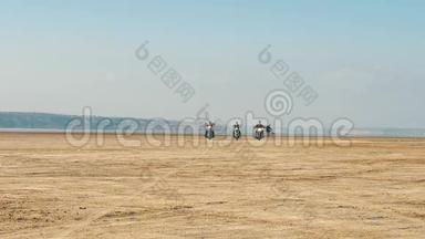 三个骑摩托车的人骑在沙滩附近的沙漠从很远。 免费乘车。