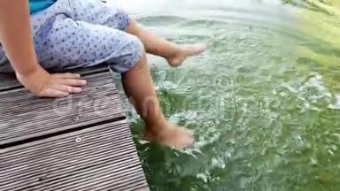 小男孩坐在河岸上用脚泼水的4K镜头。 <strong>儿童</strong>在河边<strong>游泳</strong>