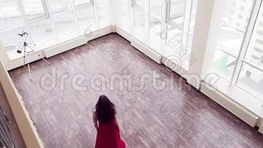一个穿着红色连衣裙的女人赤脚沿着大顶楼房间走到窗户前。 她在调戏