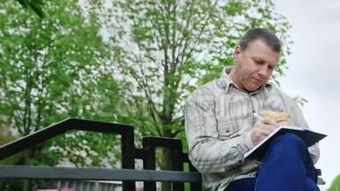 男人在公园的长椅上吃垃圾食品，在笔记本上写东西