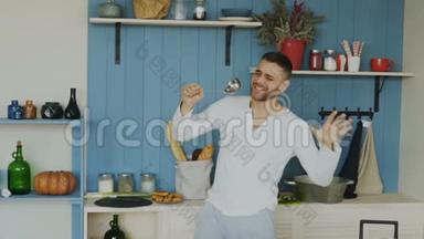 在家厨房做饭时，欢快的年轻滑稽男子用勺子跳舞唱歌