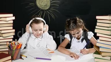 学校观念。 孩子们坐在一张桌子旁，桌子后面放着一堆书和一块黑板，上面有图纸。 孩子们玩得开心