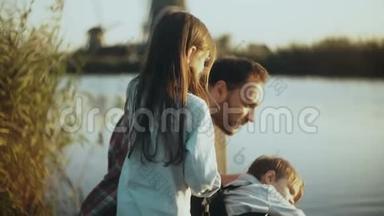 <strong>快乐</strong>的高加索家庭坐在宁静的日落湖附近。 单身父亲和两个孩子在一起度<strong>过快乐</strong>的时光。 4K特写..