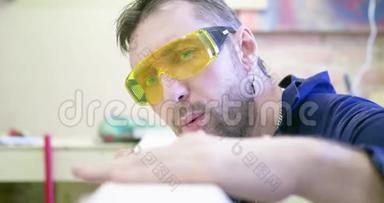 木工车间的一名男子戴着防护眼镜，用手从<strong>木屑</strong>中清理木板，并检查