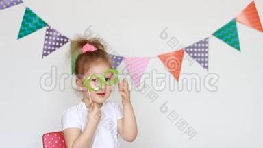 一个可爱的小女孩在浅色背景上的肖像，上面有<strong>彩色</strong>的<strong>旗子</strong>，试着装饰眼镜。