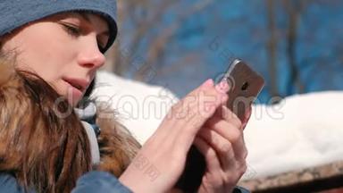 女人坐在冬<strong>季</strong>公园的<strong>手机</strong>上浏览网页。 特写的脸。