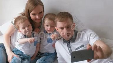 爸爸在手机上做家庭自拍。 妈妈，爸爸和两个兄弟双胞胎蹒跚学步。
