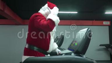 圣诞老人在健身房训练圣诞节。 圣诞老人在健身俱乐部的跑步机上跑步