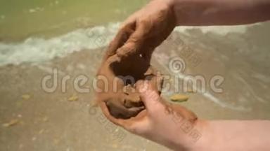 <strong>特写双手</strong>在沙滩上做粘土，沙滩和海浪为背景，夏天和旅行的概念。