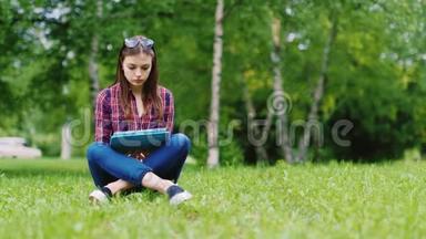 一名女学生正在<strong>准备考试</strong>。 坐在公园的草坪上，享受平板电脑