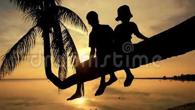 年轻快乐的父亲的<strong>剪影</strong>和他的女儿坐在棕榈树上，在惊人的<strong>金色</strong>日落。 在夏天玩得开心