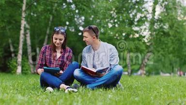 学生们坐在草地上，一个男人在看书，一个女人在用平板电脑