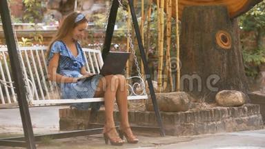 金发女郎坐在长凳上，在公园里摆着平板