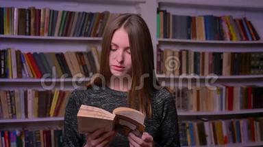 女白种人学生在书架背景上看书和观看镜头。