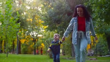 幸福家庭的概念.. 快乐的母子牵着手，奔跑着，在公园的新鲜空气中玩耍，在秋天