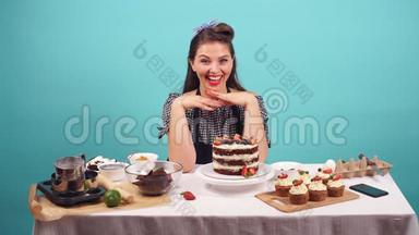 快乐的女孩糕点厨师微笑着面对相机，而坐在桌子上与糕点。