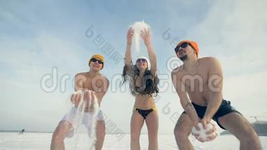 穿泳装的三个微笑的朋友在身体冷回火时玩雪。 4K.