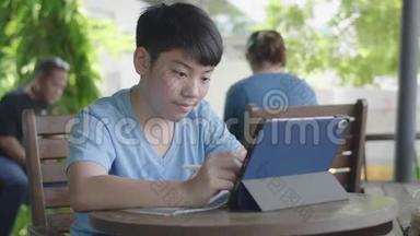 可爱的亚洲男孩使用平板电脑，年轻的十几岁男孩在数字平板电脑上做作业，默默面对。