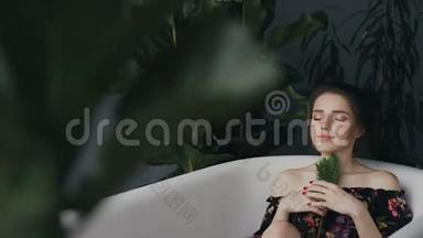 年轻女子在水疗中心的热水浴中放松。 美丽的女孩沐浴着芬芳的花朵，眼睛放松