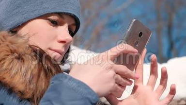 女人坐在冬<strong>季</strong>公园的<strong>手机</strong>上浏览网页。 特写脸