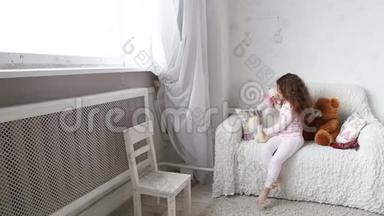 小女孩在沙发上玩玩具熊，看着窗外