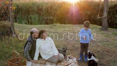 孩子在日落时分和祖母和祖父一起在<strong>小河边</strong>休息时喂狗
