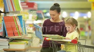 年轻的母亲和女儿在<strong>超市</strong>挑选书籍。 漂亮的女儿坐在<strong>超市</strong>的手推车里