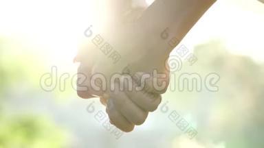 在夏季公园里，一对年轻夫妇携手并肩。 男人和女人牵着手看夕阳背景。 太阳