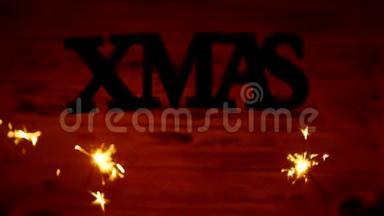 圣诞铭文XMAS自由地悬挂在空中，白色的木制背景上，火花在背景中燃烧
