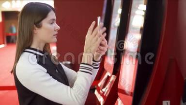 青少年从电影院的自动售货机买电影票。 女人用手机拍照片