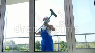 透过窗户观看，英俊<strong>的</strong>男清洁工人，穿着蓝色工作服，带着耳机，清洁，洗涤