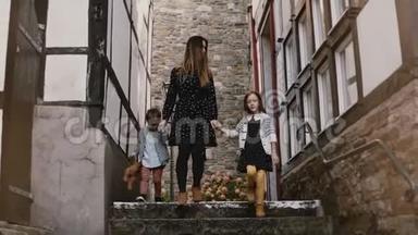 妈妈带着两个孩子走，牵着手。 女人，小男孩和女孩之间惊人的半壁江山的房子。 4K.