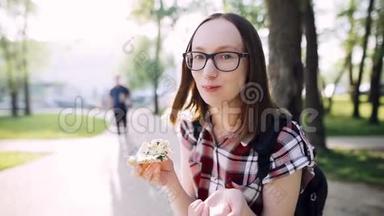 戴着眼镜和一件休闲衬衫的微笑时髦女孩吃了一片披萨。
