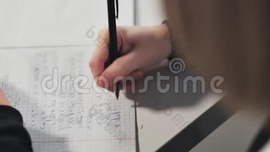 一个女学生在一本作业本中写字。 她`在做作业。