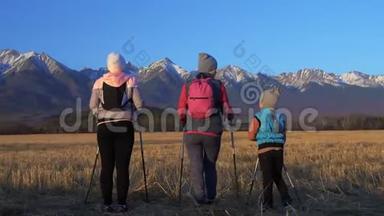 女人在大自然中行走，在田野的群山背景下。 女孩和孩子使用跋涉棒和北欧