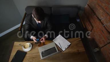 商人在咖啡馆谈论智能手机，并与商业文件合作。 男人坐在咖啡馆的桌子旁，在牢房里说话