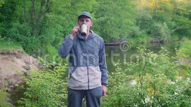 一个年轻人从森林河附近的热水瓶里喝茶