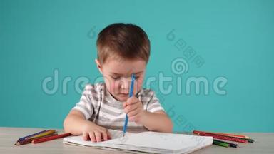 受启发的小男孩在桌子上用<strong>铅笔画画</strong>，孤立在蓝色上。