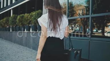 年轻漂亮聪明的商务女孩穿着商务服走路。 在这段时间里，她手里拿着包。