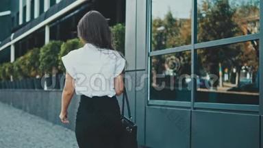 年轻漂亮聪明的商务女孩穿着商务服走路。 在这段时间里，她手里拿着包。