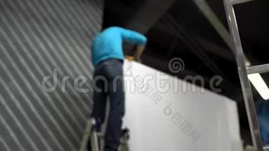 工人搭建音乐会舞台.. 穿蓝色衬衫的工人站在梯子上，安装白色的大支架，拉伸